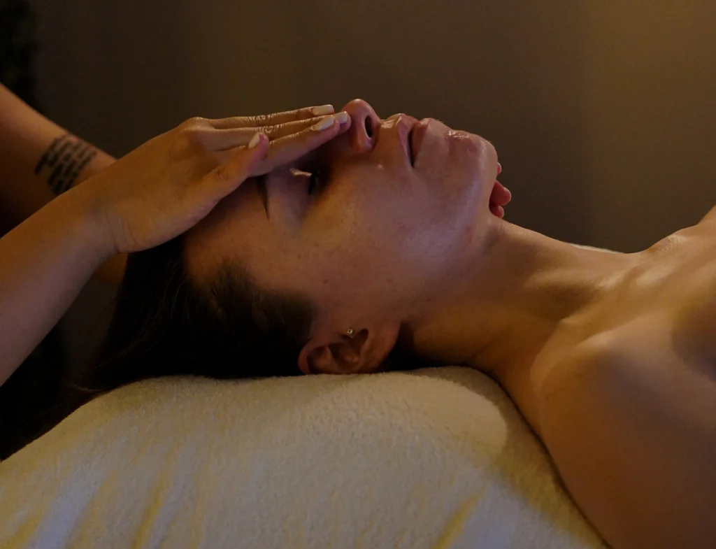 Zrelaksowana kobieta z ręką drugiej kobiety na twarzy poddawana zabiegowi facelift